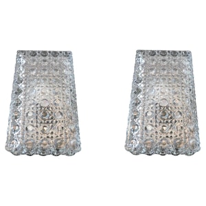 May include: Two clear, textured glass sconces with a diamond pattern. The sconces have a flared shape and are illuminated from within, creating a soft glow. The sconces are designed for wall mounting and add a touch of elegance to any space.