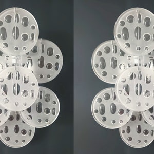 May include: Two white, circular wall sconces with a geometric pattern of holes. Each sconce has five overlapping circles with a frosted glass finish.