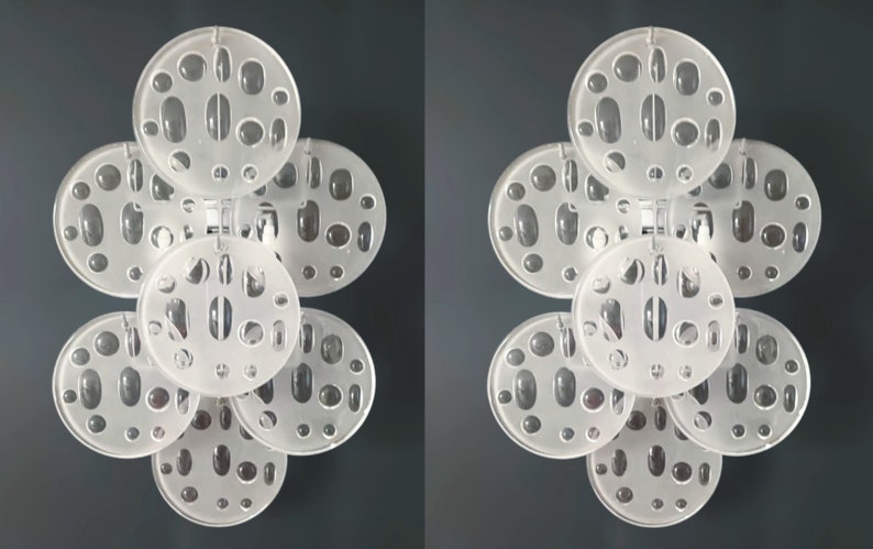 May include: Two white, circular wall sconces with a geometric pattern of holes. Each sconce has five overlapping circles with a frosted glass finish.