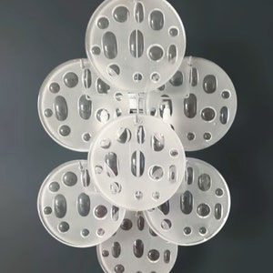 May include: A set of seven white, round, translucent, decorative wall sconces with a pattern of small, oval-shaped holes. The sconces are arranged in a cluster, with the largest sconce in the center and the smaller sconces surrounding it.