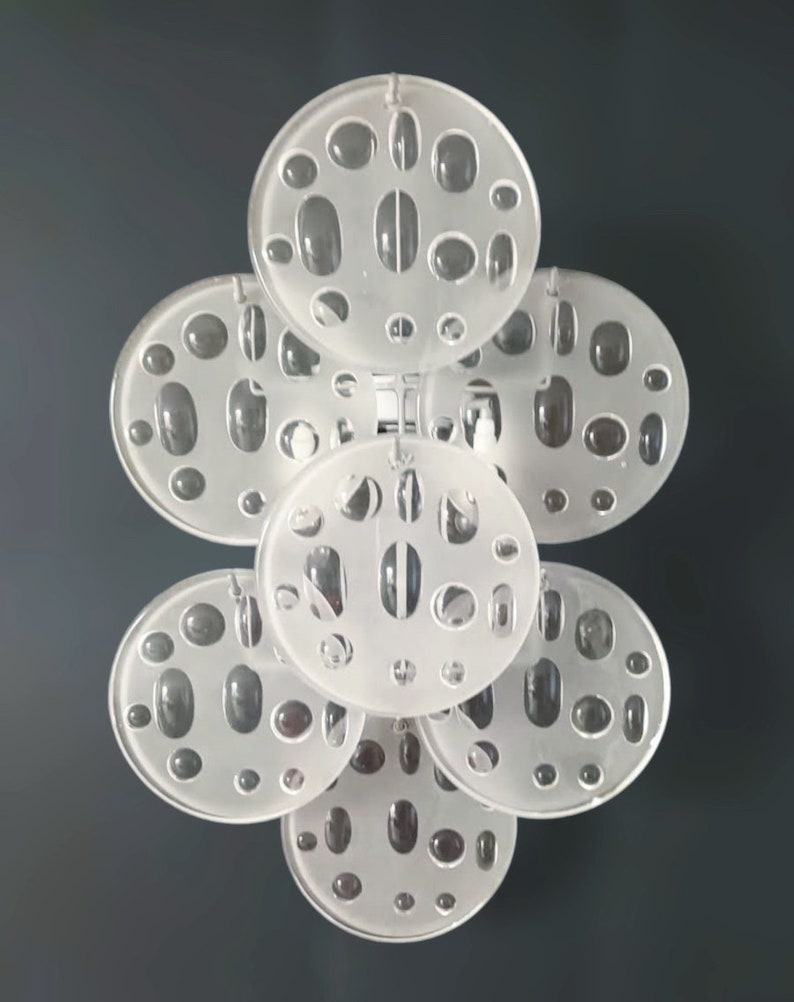 May include: A set of seven white, round, translucent, decorative wall sconces with a pattern of small, oval-shaped holes. The sconces are arranged in a cluster, with the largest sconce in the center and the smaller sconces surrounding it.