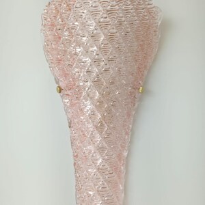 May include: A pink glass wall sconce with a textured, diamond-shaped pattern. The sconce has a gold metal mounting bracket.