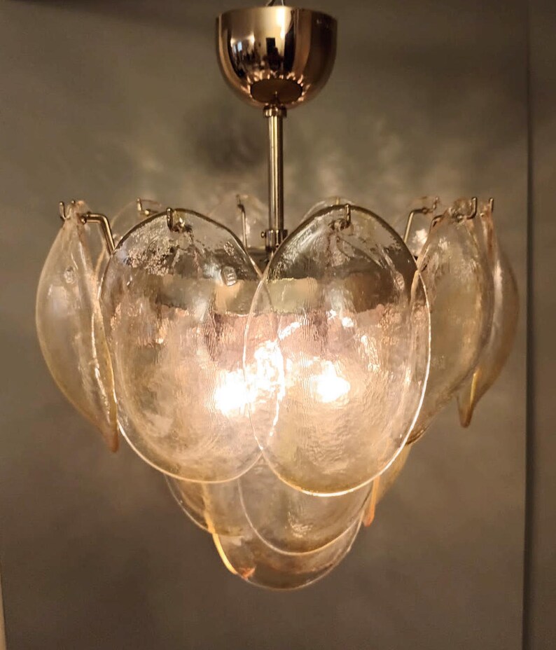 May include: A vintage chandelier with a gold-toned metal frame and multiple petal-shaped glass shades. The glass shades are a light amber color and have a textured surface. The light fixture is suspended from a gold-colored ceiling mount.