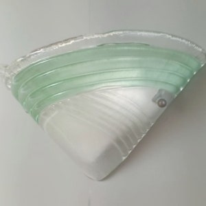 May include: A white and green glass wall sconce with a textured design. The sconce has a triangular shape and a single light bulb.