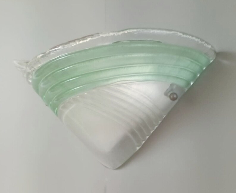 May include: A white and green glass wall sconce with a textured design. The sconce has a triangular shape and a single light bulb.