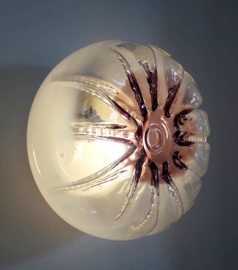 Pu&ograve; includere: Un globo di vetro trasparente con un motivo a stella testurizzato in una tonalit&agrave; viola scuro. Il globo &egrave; illuminato dall'interno, creando un bagliore morbido.