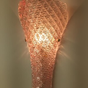 May include: A pink glass wall sconce with a textured, bubble-like design. The sconce is lit with a light bulb, casting a warm glow.