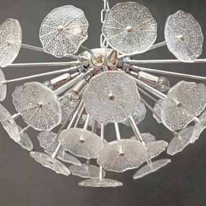 May include: A chrome and glass chandelier with multiple clear glass flower-shaped shades. The chandelier has a modern design and is perfect for a contemporary home.