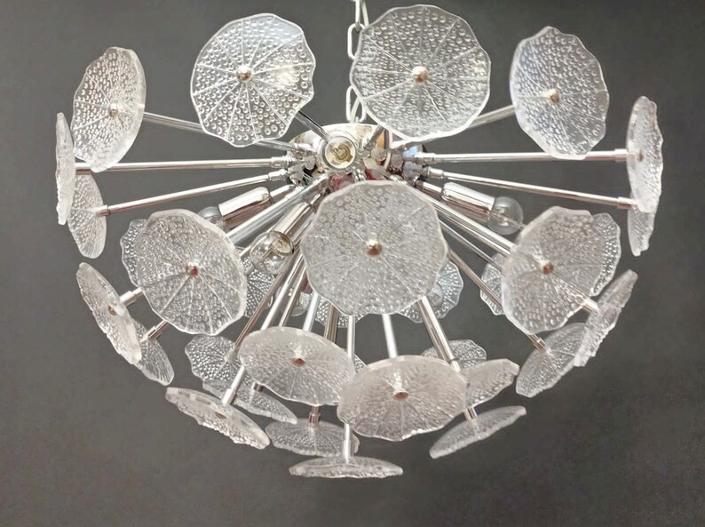 May include: A chrome and glass chandelier with multiple clear glass flower-shaped shades. The chandelier has a modern design and is perfect for a contemporary home.
