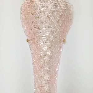May include: A pink glass wall sconce with a textured, diamond-shaped pattern. The sconce has a scalloped top and is mounted on a white wall.