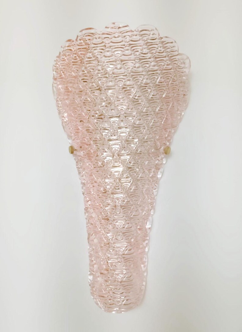 May include: A pink glass wall sconce with a textured, diamond-shaped pattern. The sconce has a scalloped top and is mounted on a white wall.