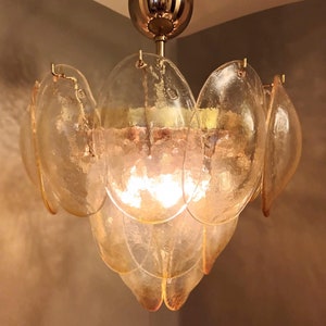 May include: A vintage-style chandelier with a flower-like design. The fixture features multiple layers of amber-colored, petal-shaped glass shades. The central light source is visible, and the fixture is suspended from a gold-toned ceiling mount.