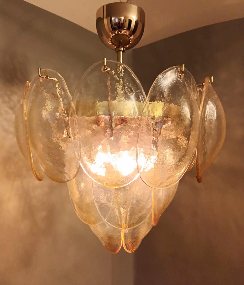 May include: A vintage-style chandelier with a flower-like design. The fixture features multiple layers of amber-colored, petal-shaped glass shades. The central light source is visible, and the fixture is suspended from a gold-toned ceiling mount.