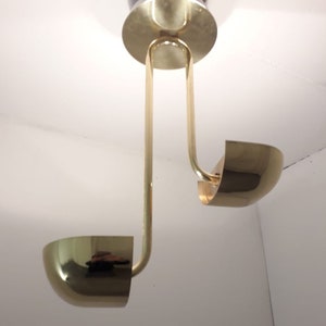 May include: A brass ceiling light fixture with two curved arms and round shades. The fixture is suspended from the ceiling by a single rod.