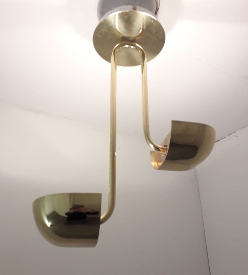 May include: A brass ceiling light fixture with two curved arms and round shades. The fixture is suspended from the ceiling by a single rod.