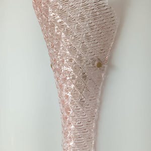 May include: A pink glass wall sconce with a textured, wavy design. The sconce has a cone shape and is attached to the wall with two gold-colored brackets.
