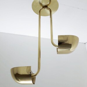 May include: A gold-toned, two-light pendant lamp with a unique design. The lamp features two curved, bowl-shaped shades and a central, circular canopy.