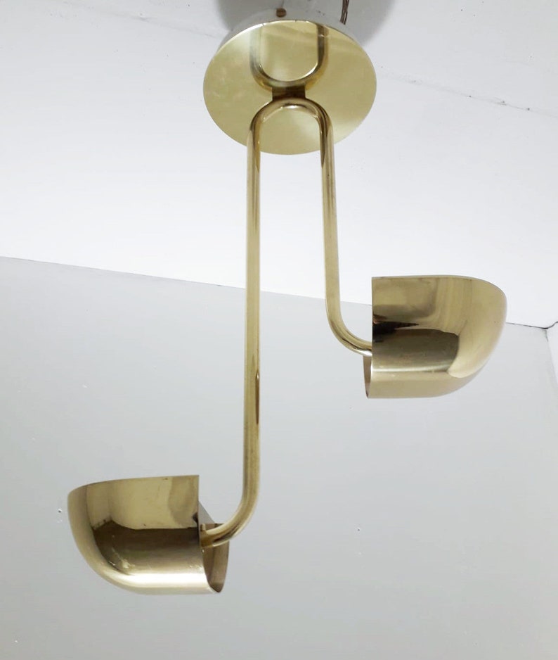 May include: A gold-toned, two-light pendant lamp with a unique design. The lamp features two curved, bowl-shaped shades and a central, circular canopy.