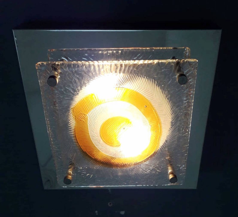 May include: A square ceiling light fixture with a frosted glass shade featuring a concentric circle design in shades of yellow and white.