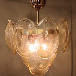 May include: A vintage chandelier with a gold-toned metal frame and multiple petal-shaped glass shades. The glass shades are a warm amber color, and the light bulbs are visible inside. The fixture is designed to be mounted on a ceiling.