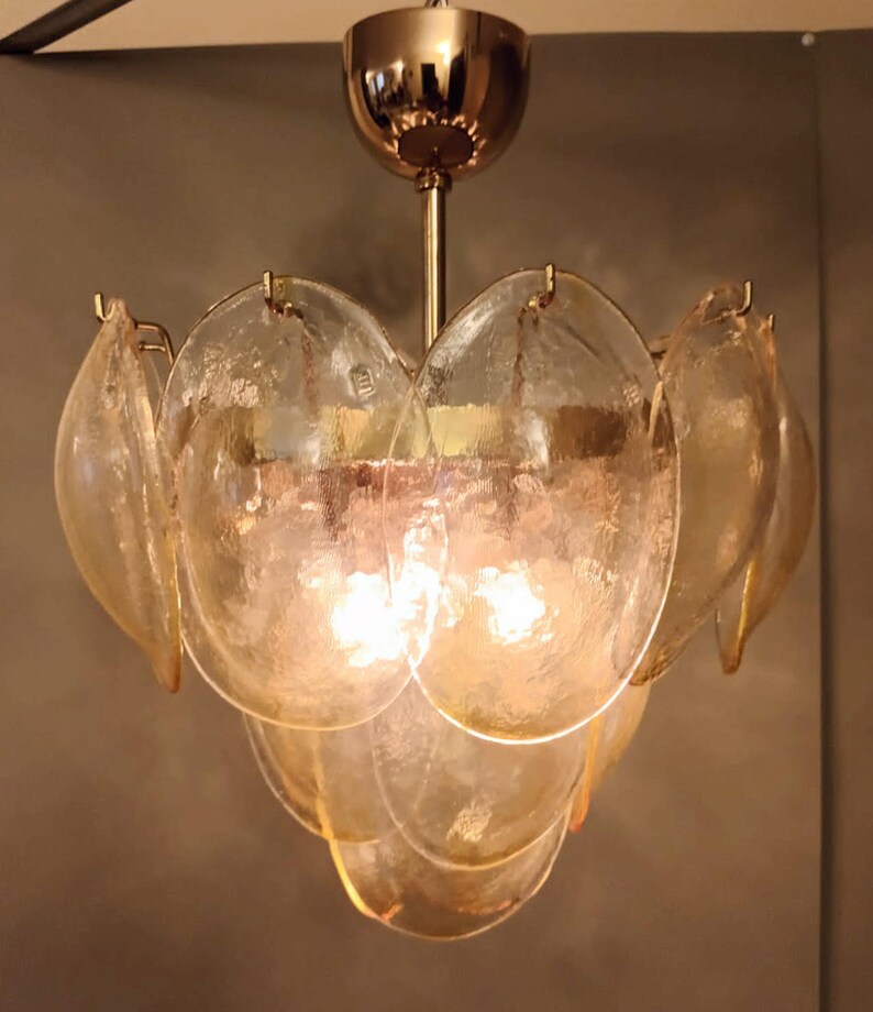 May include: A vintage chandelier with a gold-toned metal frame and multiple petal-shaped glass shades. The glass shades are a warm amber color, and the light bulbs are visible inside. The fixture is designed to be mounted on a ceiling.