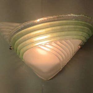 May include: A white and green glass wall sconce with a frosted glass shade and a decorative design.