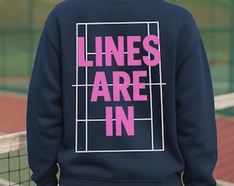 May include: Navy blue sweatshirt with the words "LINES ARE IN" in pink, inside a white tennis court outline. The sweatshirt is a solid color, and the text is bold and easy to read. The design is on the back of the sweatshirt.