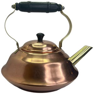 Może przedstawiać: Kociołek miedziany z uchwytem i wylewką z mosiądzu. Kociołek ma czarny drewniany uchwyt i błyszczące miedziane wykończenie.