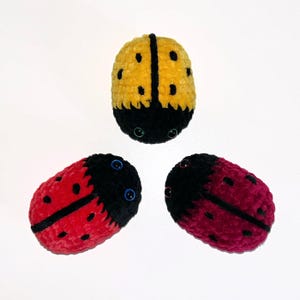 May include: Three crocheted ladybug toys. One is yellow, one is red, and one is burgundy. Each ladybug has black spots and black yarn for the head and legs.