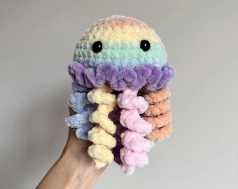 May include: A handmade, plush jellyfish toy in a rainbow of colors. The top is a blend of yellow, green, and pink, with black button eyes. The tentacles are in shades of blue, yellow, pink, and orange. A soft, cuddly, and whimsical toy.