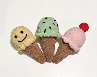 May include: Three crocheted ice cream cones, one yellow with a smiley face, one green with chocolate sprinkles, and one pink with a red cherry on top.