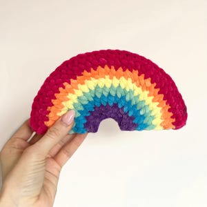 Op de afbeelding: Een gehaakte regenboog gemaakt van kleurrijk garen. De regenboog is een pluche, zacht en kleurrijk woonaccessoire.