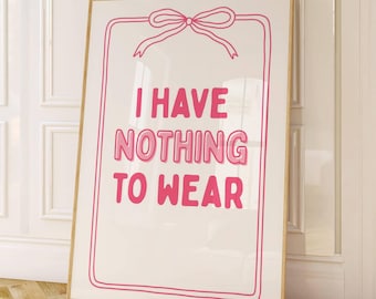 May include: A framed art print with the text "I HAVE NOTHING TO WEAR" in pink, set against a white background. The text is enclosed within a pink border with a bow at the top. The frame is a light brown color.