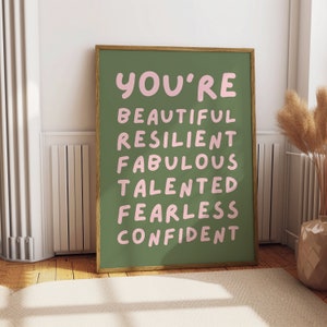 Op de afbeelding: Een ingelijst print met een groene achtergrond en roze tekst die "You're Beautiful Resilient Fabulous Talented Fearless Confident" zegt.