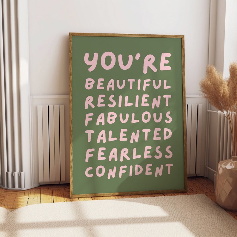 Op de afbeelding: Een ingelijst print met een groene achtergrond en roze tekst die "You're Beautiful Resilient Fabulous Talented Fearless Confident" zegt.