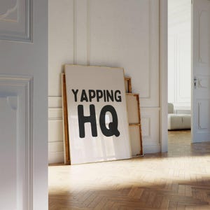 May include: A white framed poster with the text "YAPPING HQ" in black lettering.