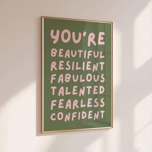 Op de afbeelding: Een groene poster met een lijst, met de tekst "You're" in roze, gevolgd door de woorden "Beautiful, Resilient, Fabulous, Talented, Fearless, Confident" in roze.