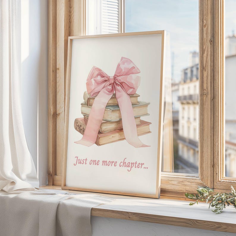 May include: A framed print featuring a watercolour illustration of a stack of books tied with a pink ribbon bow. The text "Just one more chapter..." is printed below the books.