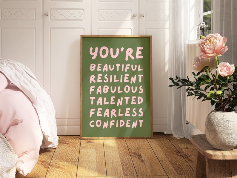 Op de afbeelding: Een groene poster met een lijst met positieve woorden in roze: beautiful, resilient, fabulous, talented, fearless, confident.