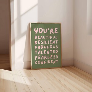 Op de afbeelding: Een groene poster met een lijst met positieve woorden in roze: beautiful, resilient, fabulous, talented, fearless, confident.