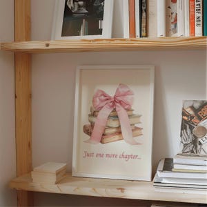 May include: A white framed print featuring a pink bow atop a stack of books. The text "Just one more chapter..." is beneath the books.