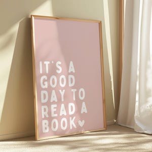 May include: A framed pink poster with the text "It's a good day to read a book" in white with a heart symbol.