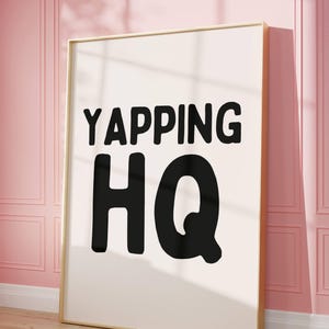 May include: A white framed poster with black text that reads "YAPPING HQ" on a pink wall.
