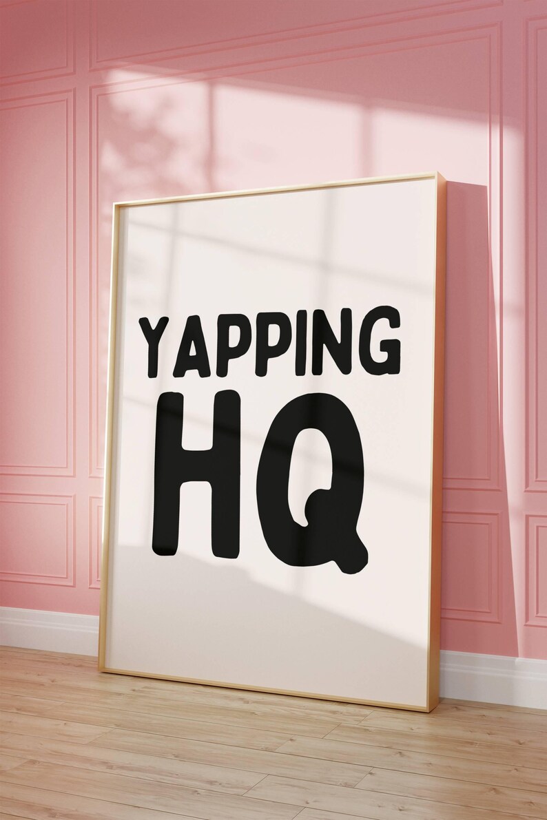 May include: A white framed poster with black text that reads "YAPPING HQ" on a pink wall.
