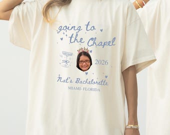 May include: Cream-colored t-shirt with the text "going to the Chapel" in blue script, along with a photo and the text "Nat's Bachelorette Miami-Florida 2026". The shirt features a champagne glass graphic.