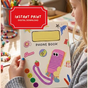 May include: A white phone book with a yellow rectangular label and the text "PHONE BOOK" printed in black. The cover features colorful stickers including a pink telephone, a strawberry, smiley faces, and a blue dolphin. The top includes a red banner with the text "INSTANT PRINT DIGITAL DOWNLOAD".