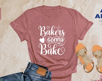 Könnte beinhalten: Ein T-Shirt in Heide-Mauve mit dem Text "Bakers gonna bake" in Weiß. Der Text ist in einer kursivschriftlichen Schriftart und enthält Herzen und Schnörkel.