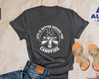 May include: Heather dark gray t-shirt with the text "LIFE IS BETTER AROUND THE CAMPFIRE" in a white circular design. The image also includes blue jeans, sandals, and the Alpine Design logo.