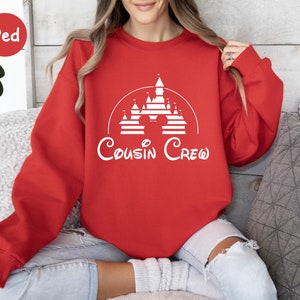 Pode incluir: Camisola vermelha com um gr&aacute;fico branco de um castelo e orelhas do Mickey Mouse com o texto "Cousin Crew".