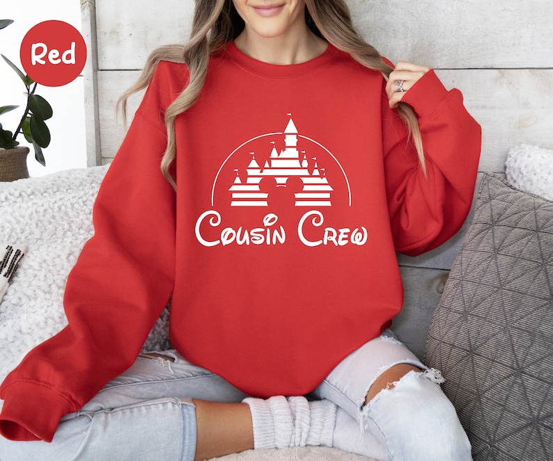 Pode incluir: Camisola vermelha com um gr&aacute;fico branco de um castelo e orelhas do Mickey Mouse com o texto "Cousin Crew".